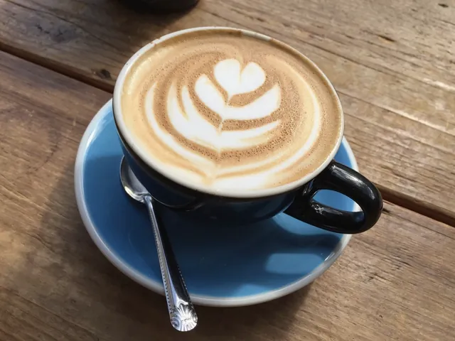A latte with leaf-shaped foam art in a blue cup